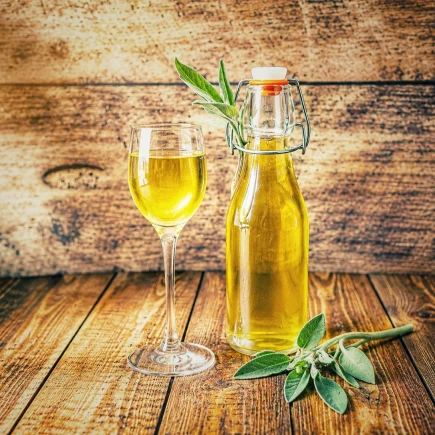 Selbstgemachter Salbeisirup in einer Glasflasche mit Bügelverschluss und einem gefüllten Glas auf rustikalem Holztisch