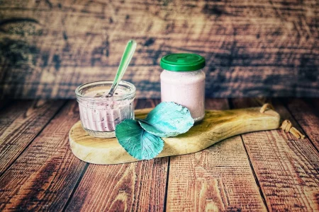 Rotkohl-Pesto mit Pinienkernen in einem Glas und einem kleinen Schälchen auf einem Holzbrett, dekoriert mit frischen Rotkohlblättern.