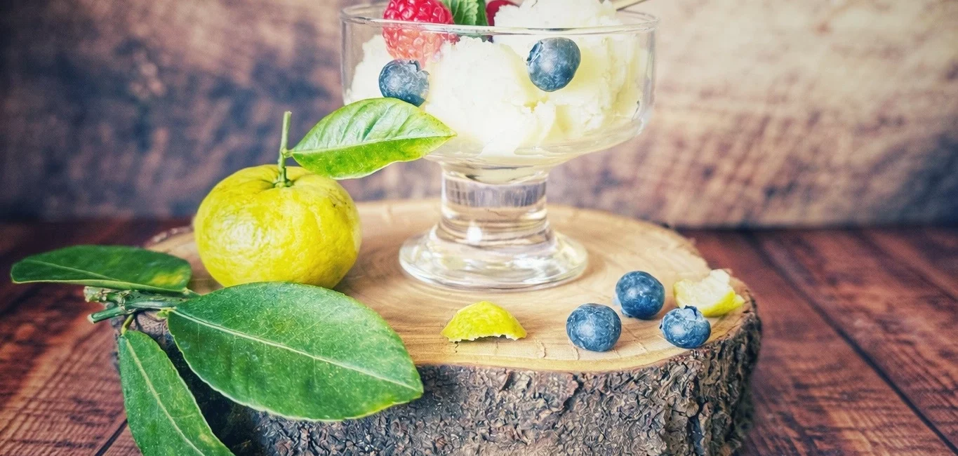 Glas mit Joghurt-Eis, garniert mit Himbeeren, Blaubeeren und Minze, auf einer Holzscheibe mit Pursha-Limetten und Blättern