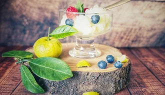 Glas mit Joghurt-Eis, garniert mit Himbeeren, Blaubeeren und Minze, auf einer Holzscheibe mit Pursha-Limetten und Blättern