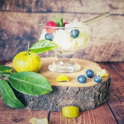 Glas mit Joghurt-Eis, garniert mit Himbeeren, Blaubeeren und Minze, auf einer Holzscheibe mit Pursha-Limetten und Blättern