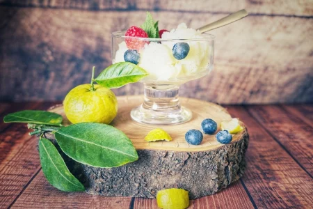 Glas mit Joghurt-Eis, garniert mit Himbeeren, Blaubeeren und Minze, auf einer Holzscheibe mit Pursha-Limetten und Blättern