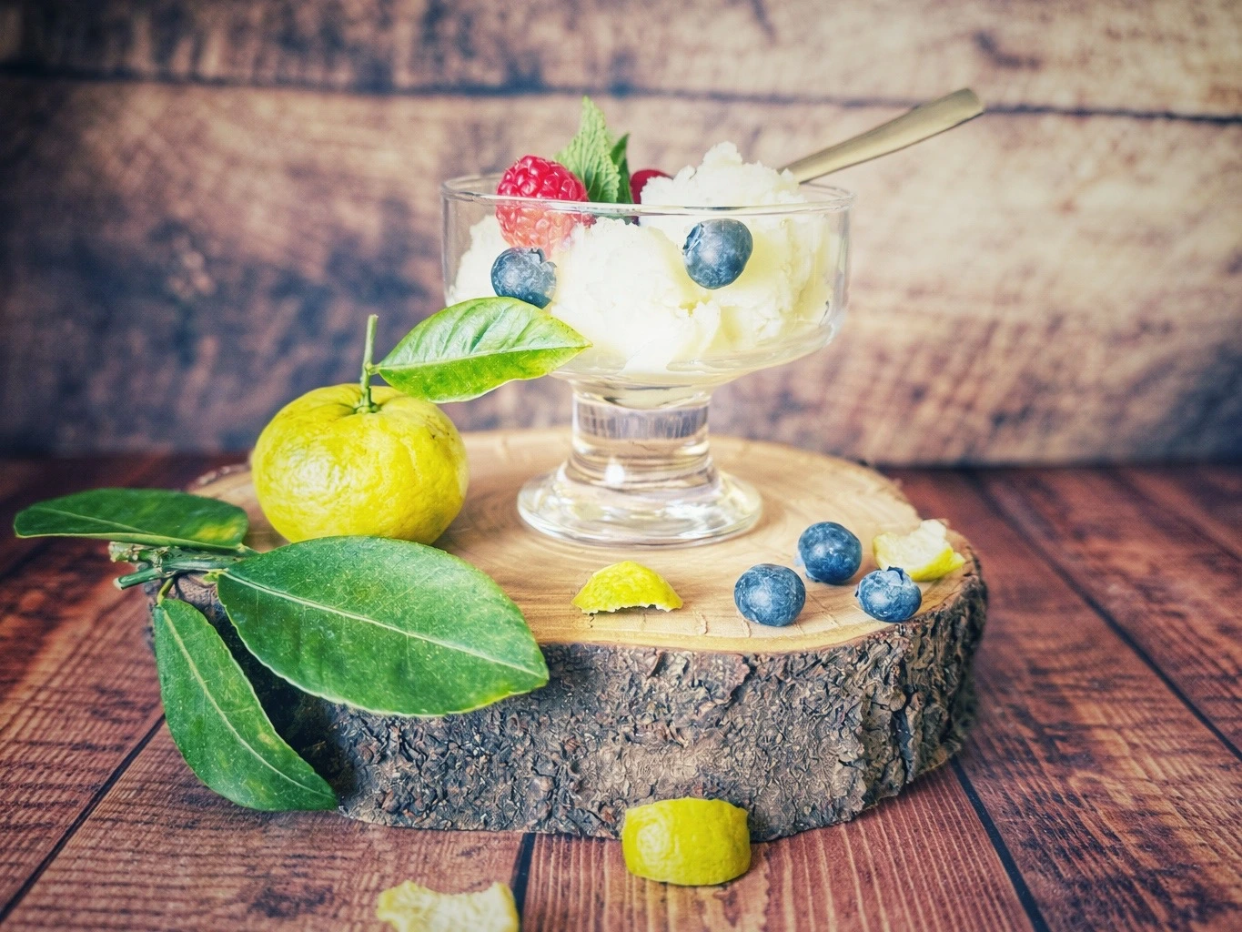 Glas mit Joghurt-Eis, garniert mit Himbeeren, Blaubeeren und Minze, auf einer Holzscheibe mit Pursha-Limetten und Blättern