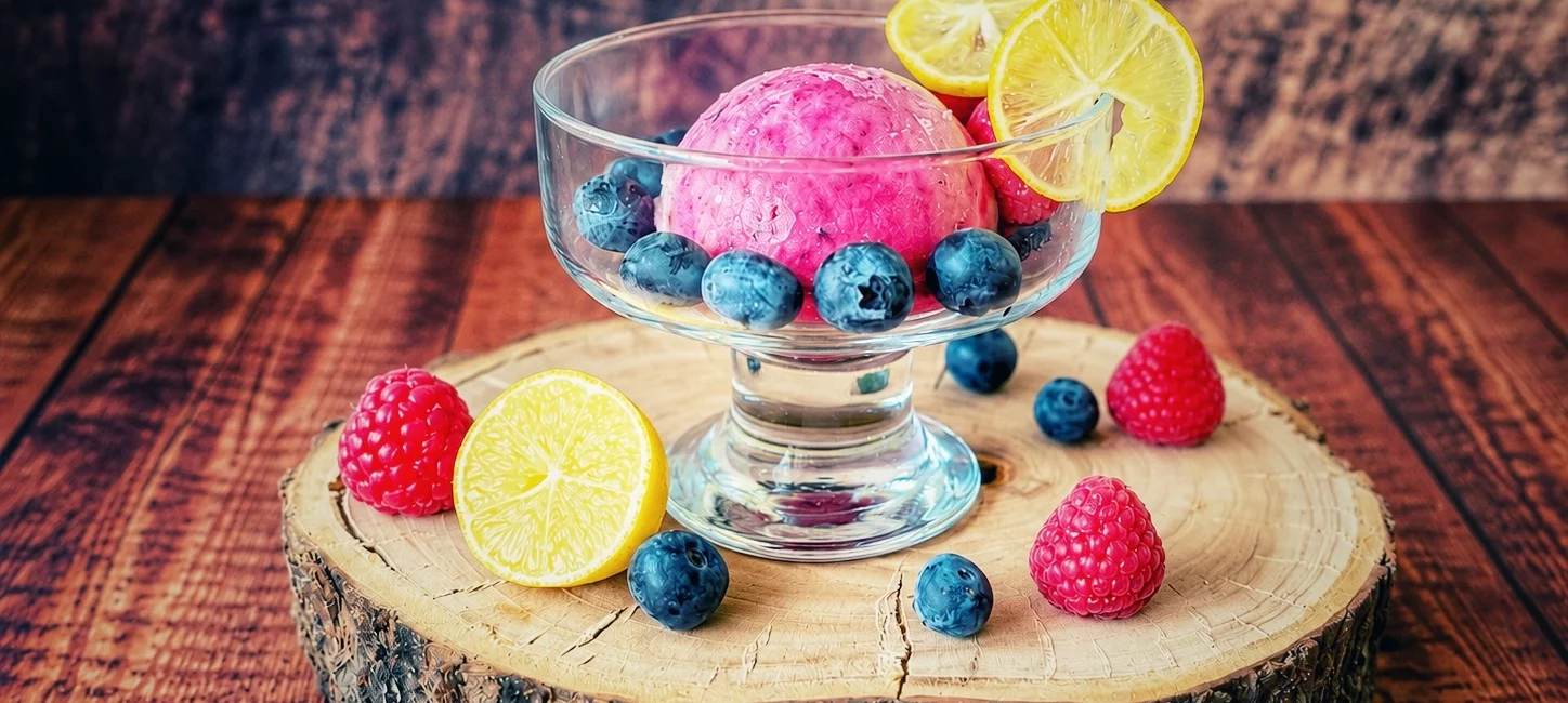 Limequat-Beeren-Eis in einer Glasschale mit Heidelbeeren, Himbeeren und Limequat-Scheiben auf einer Holzscheibe