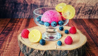 Limequat-Beeren-Eis in einer Glasschale mit Heidelbeeren, Himbeeren und Limequat-Scheiben auf einer Holzscheibe