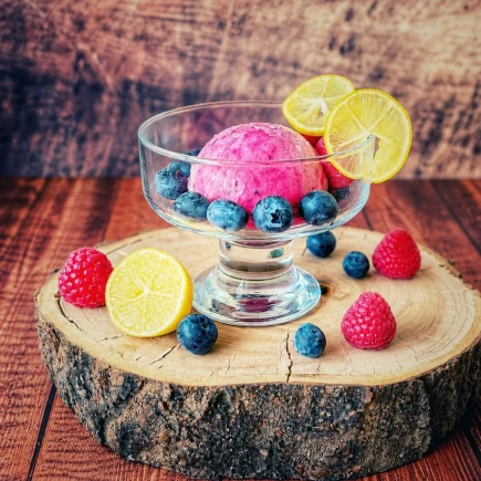 Limequat-Beeren-Eis in einer Glasschale mit Heidelbeeren, Himbeeren und Limequat-Scheiben auf einer Holzscheibe