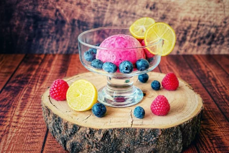 Limequat-Beeren-Eis in einer Glasschale mit Heidelbeeren, Himbeeren und Limequat-Scheiben auf einer Holzscheibe