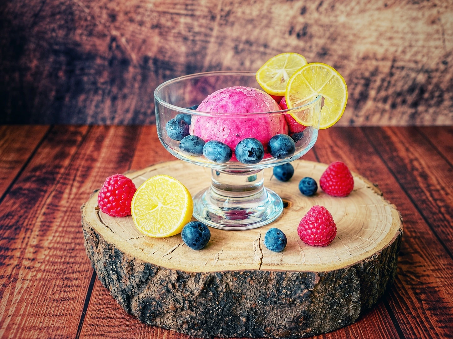 Limequat-Beeren-Eis in einer Glasschale mit Heidelbeeren, Himbeeren und Limequat-Scheiben auf einer Holzscheibe