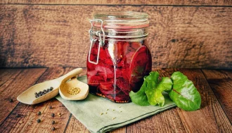 S&uuml;&szlig;-sauer eingelegte Rote Bete in einem verschlossenen B&uuml;gelglas auf einem rustikalen Holztisch, dekoriert mit frischen Rote-Bete-Bl&auml;ttern und Gew&uuml;rzen.