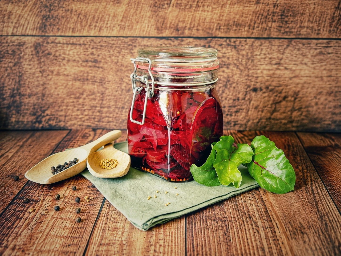 Süß-sauer eingelegte Rote Bete in einem verschlossenen Bügelglas auf einem rustikalen Holztisch, dekoriert mit frischen Rote-Bete-Blättern und Gewürzen.