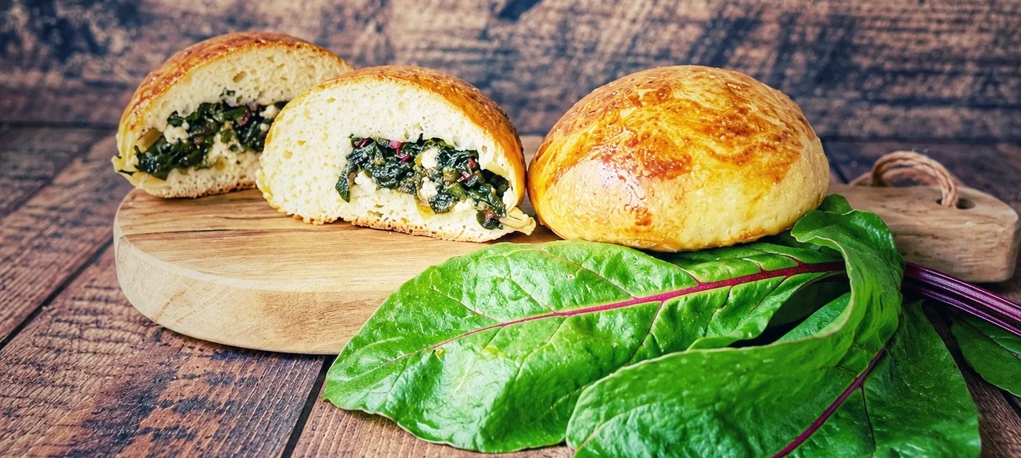 Gef&uuml;llte Br&ouml;tchen mit Rote-Bete-Bl&auml;ttern und Feta auf einem Holzbrett