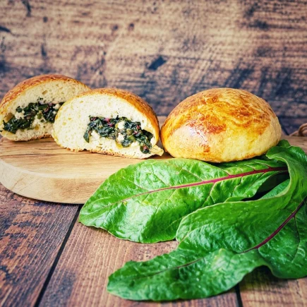 Gef&uuml;llte Br&ouml;tchen mit Rote-Bete-Bl&auml;ttern und Feta auf einem Holzbrett