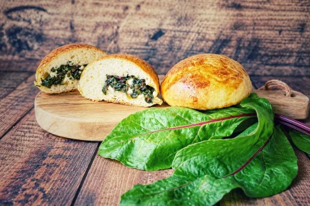 Gef&uuml;llte Br&ouml;tchen mit Rote-Bete-Bl&auml;ttern und Feta auf einem Holzbrett