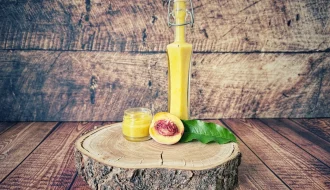 Zwergpfirsich-Dressing in einer B&uuml;gelflasche mit kleinem Glas und halbiertem Pfirsich auf einer Holzscheibe