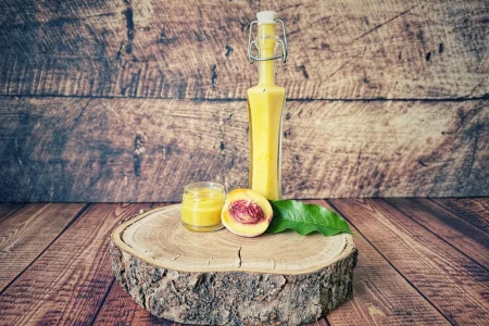 Zwergpfirsich-Dressing in einer Bügelflasche mit kleinem Glas und halbiertem Pfirsich auf einer Holzscheibe